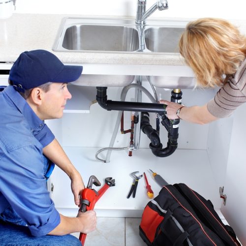Mature plumber fixing a sink at kitchen
